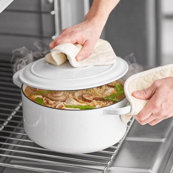 A person using a white Valor enameled cast iron Dutch oven to cook on a stove.