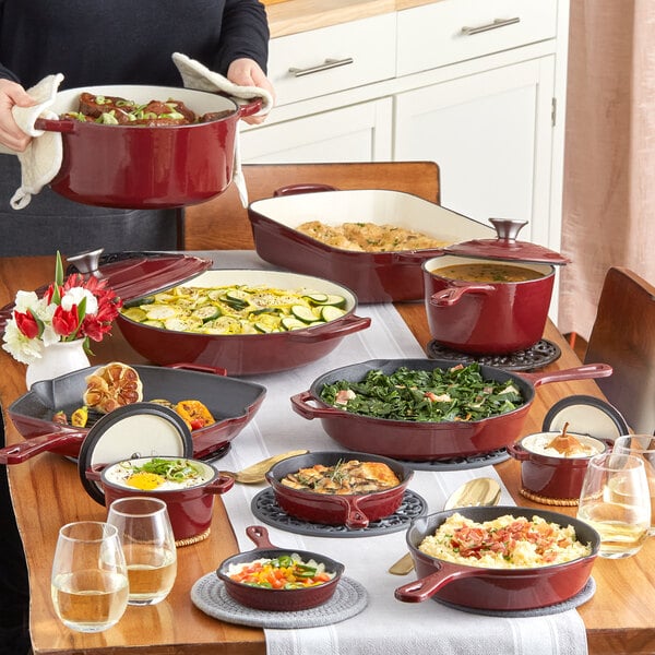 A woman serving food from a Valor Merlot Enameled Cast Iron Dutch Oven on a table full of food.
