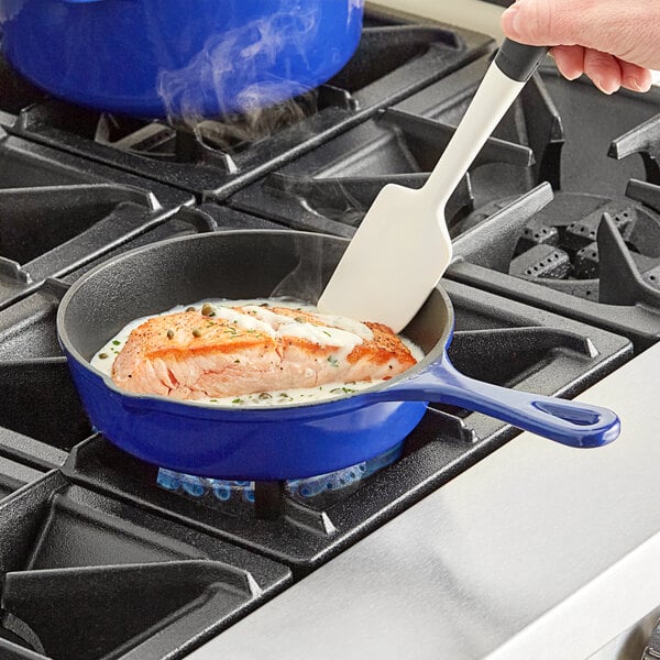 A person cooking salmon in a blue Valor enameled cast iron skillet on a stove.