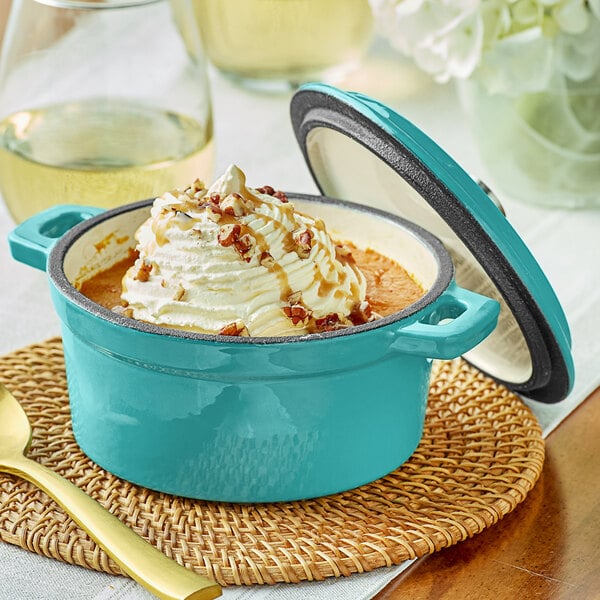 A Valor Aqua Sky enameled cast iron pot with a lid, filled with sauce and a spoon on a bowl of ice cream.