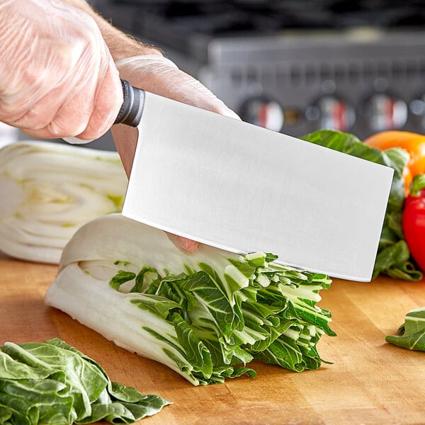 A person using a Mercer Culinary Chinese Cleaver Chef's Knife to cut vegetables on a cutting board.