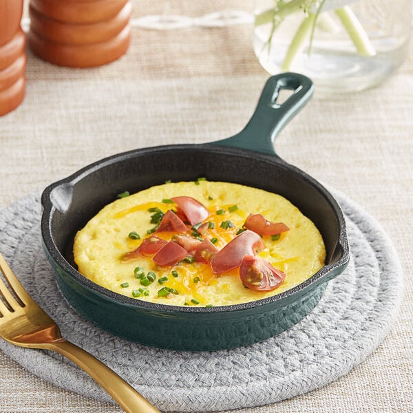 A Valor green enameled mini cast iron skillet with an omelette with tomatoes and green onions in it.