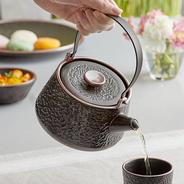 A hand pouring water into a black Acopa Heika teapot.