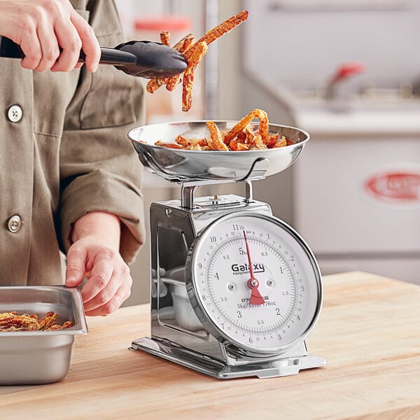 A woman using a Galaxy portion scale to weigh food in a stainless steel bowl.