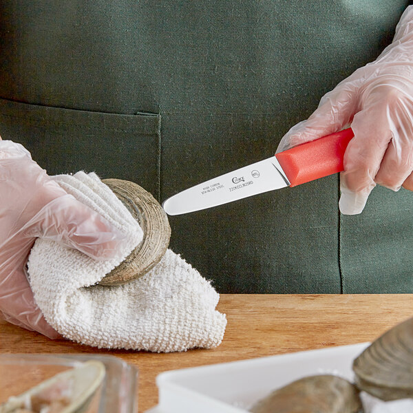 A person with gloves using a Choice stainless steel clam knife with a red handle to cut a clam.