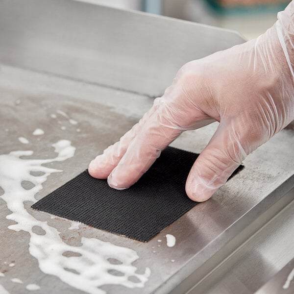 A person wearing clear gloves cleaning a metal surface with Scrubble by ACS black grill screens.