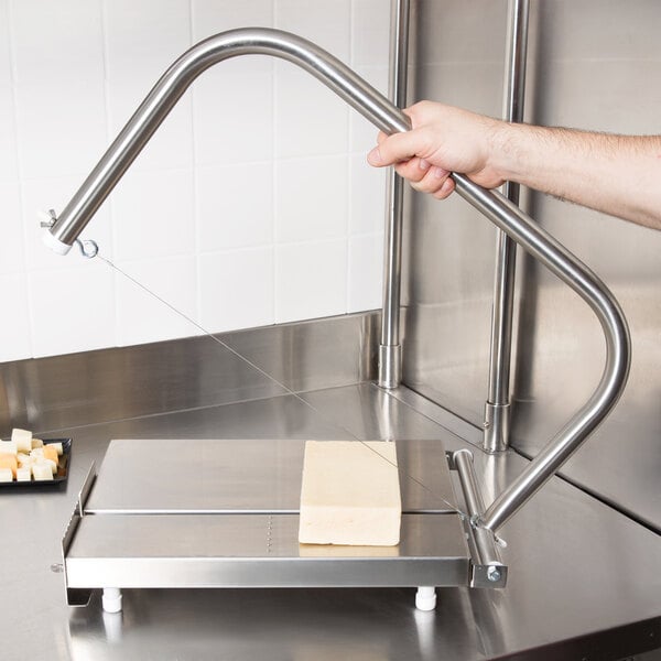 A hand using a Vollrath Redco Cheese Blocker to cut cheese on a machine.