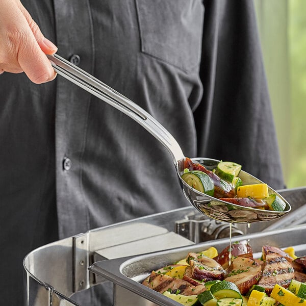 A person using a Vollrath stainless steel slotted oval serving spoon to serve food from a bowl.