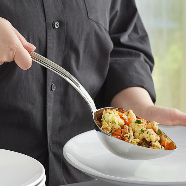 A person using a Vollrath stainless steel oval serving spoon to serve food from a bowl.