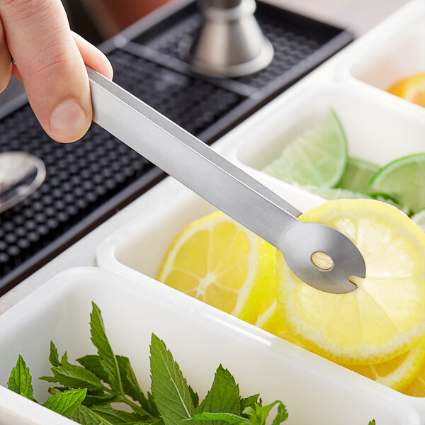 A person using American Metalcraft stainless steel bar tongs to pick up a slice of lemon from a tray.