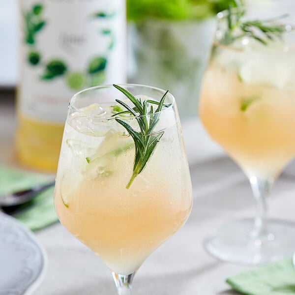 a glass of drink with a sprig of rosemary