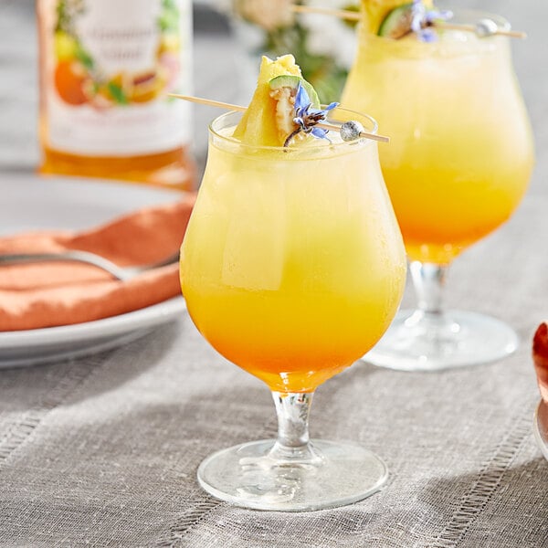 Two glasses of yellow liquid with pineapple on a table.