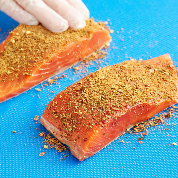 A hand seasoning a piece of salmon with Old Bay Rub.