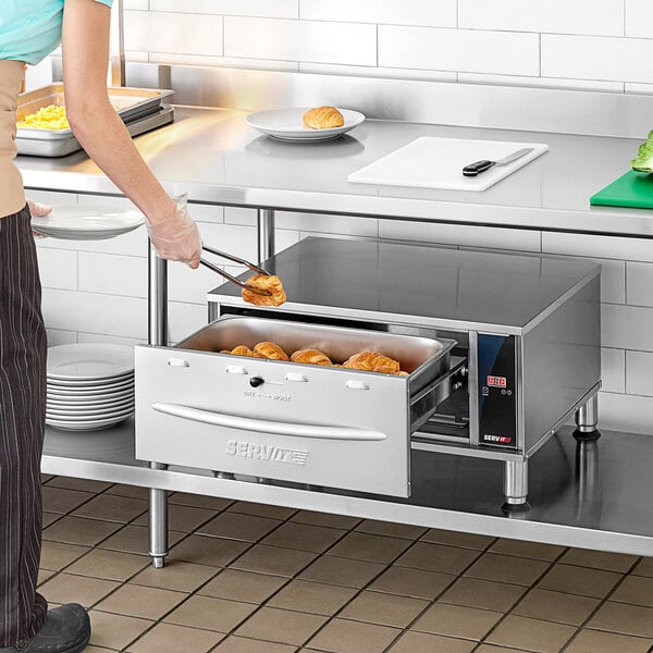 A woman using a ServIt freestanding drawer warmer to hold food on a tray.