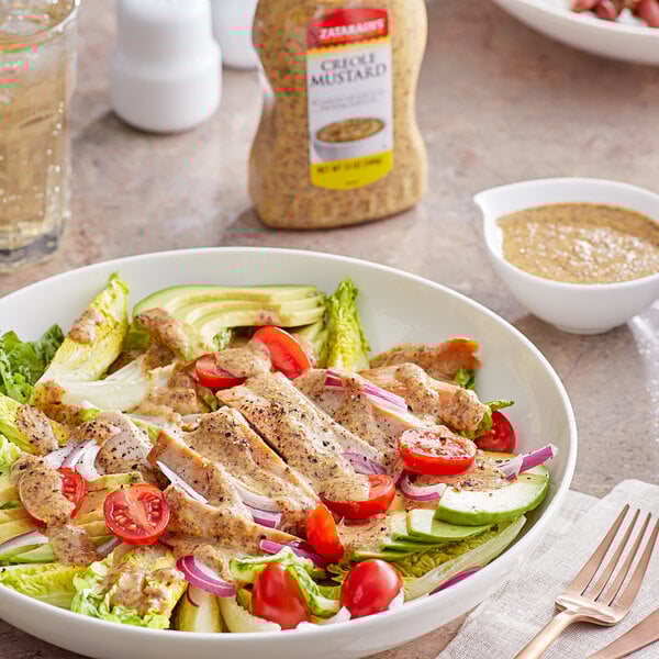 A bowl of salad with lettuce, chicken, and Zatarain's Creole Mustard on a table.
