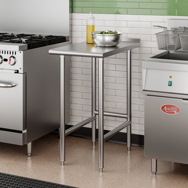An Advance Tabco stainless steel filler table in a kitchen with stainless steel appliances.
