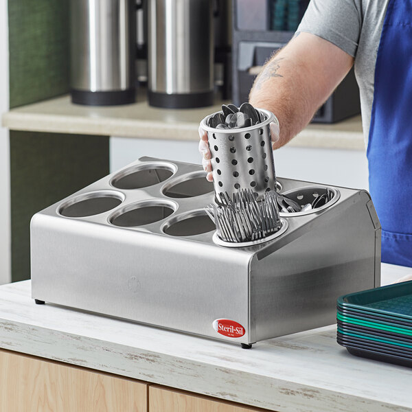 A man using a Steril-Sil stainless steel countertop flatware organizer to put utensils away on a school kitchen counter.