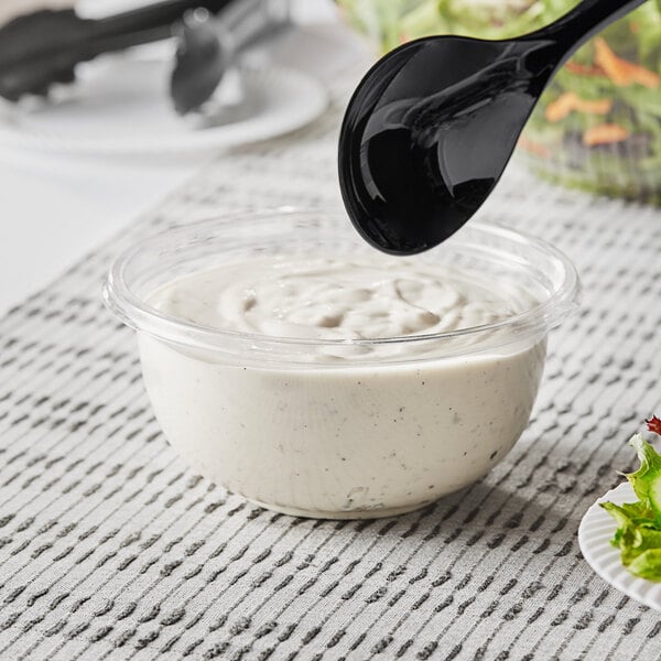 A black spoon serving white sauce from a clear plastic bowl.