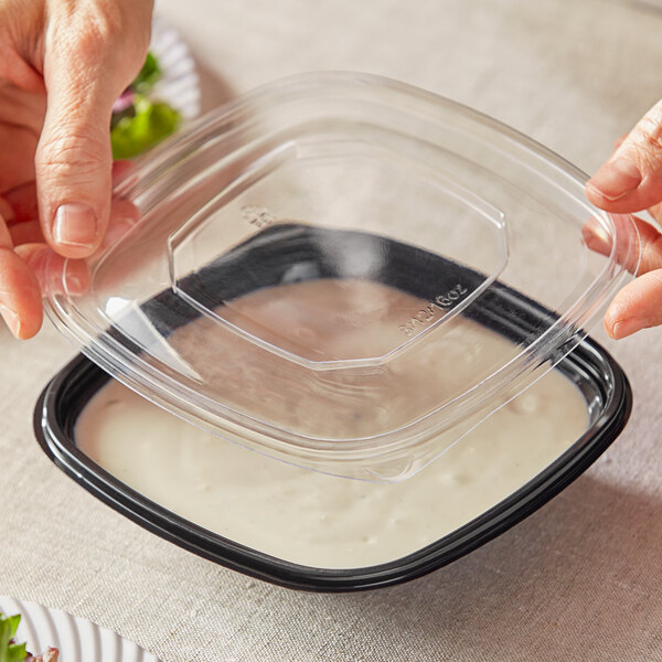 A person holding a Visions clear plastic bowl with a clear flat lid.