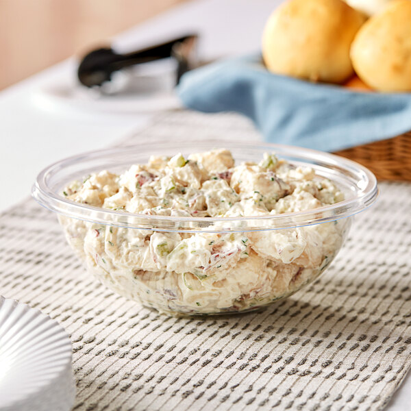 A clear plastic Visions serving bowl filled with food on a table.