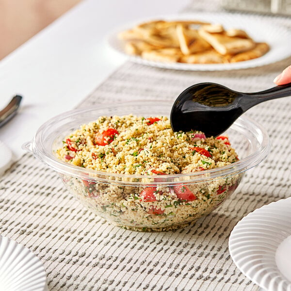 A person holding a spoon over a bowl of food with a Visions clear plastic bowl on a table.