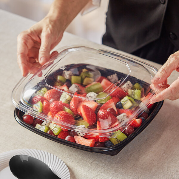 A person holding a Visions clear plastic container with a fruit salad inside.