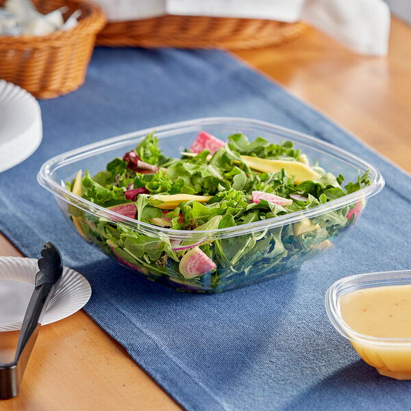 A Visions clear plastic bowl filled with salad on a table.