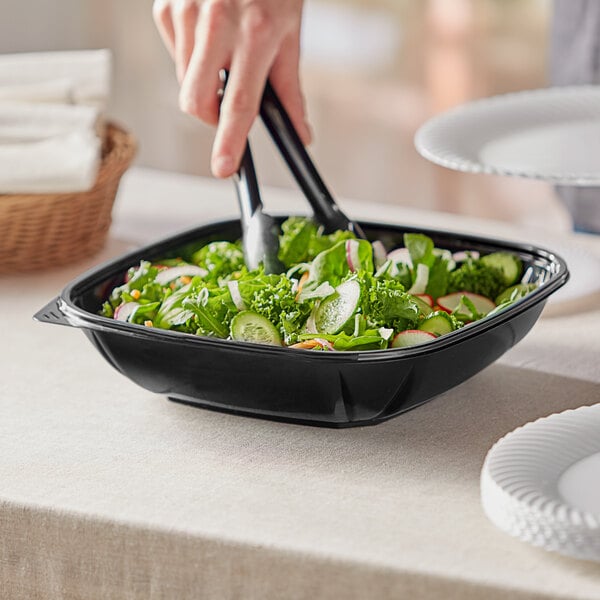 A hand holding a Visions black bowl filled with salad.