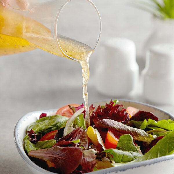 A person pouring AAK Select Recipe Traditional Italian Dressing into a bowl of salad.