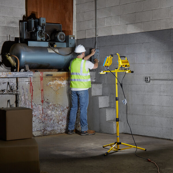 A man wearing a reflective safety vest and hard hat working on a piece of equipment with a Voltec LED work light.