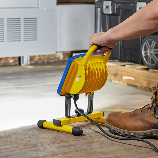 A person using a Voltec Portable LED work light with a yellow handle to repair a floor.