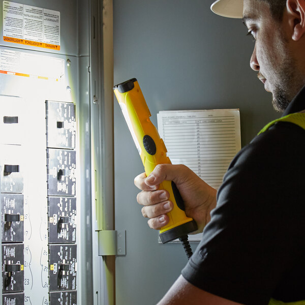 Electrician using a handheld light to look at an electrical panel