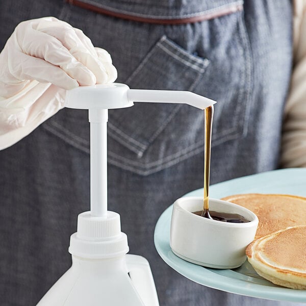 A person using a white Tablecraft condiment pump to pour syrup over a dish of pancakes.
