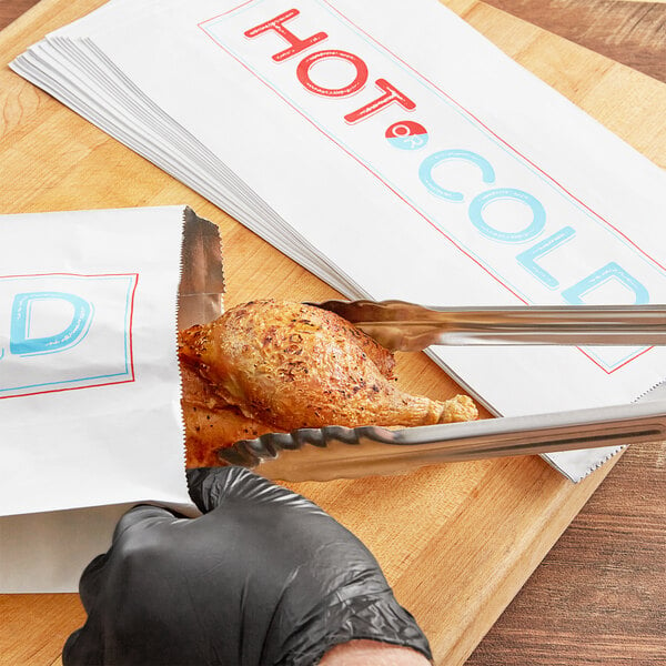 A person using tongs to put a piece of chicken in a Choice insulated foil bag.