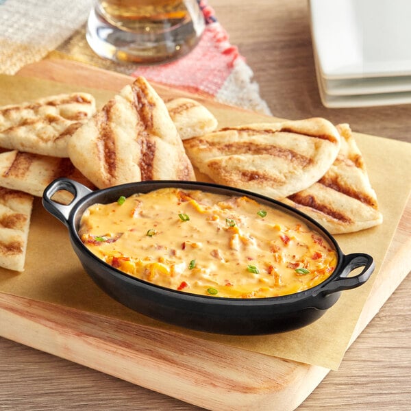 An American Metalcraft black faux cast iron melamine casserole dish with food on a table.