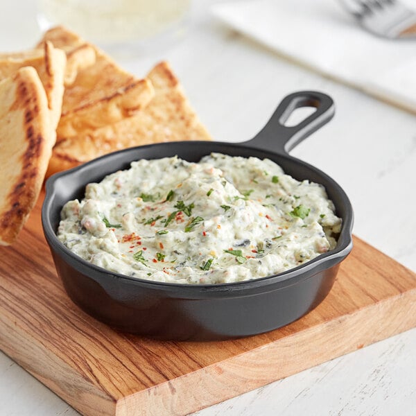 A bowl of dip in an American Metalcraft black faux cast iron fry pan server with pita bread on a cutting board.