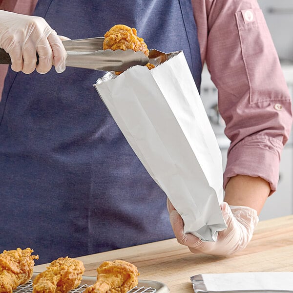 A person holding a Carnival King unprinted foil bag of fried chicken.