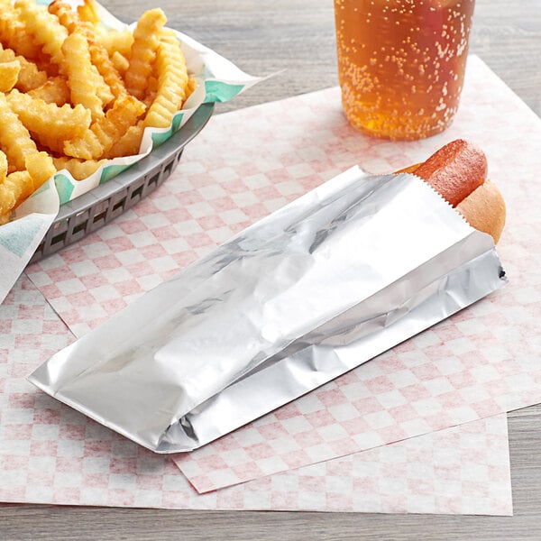 A hot dog in a Carnival King foil bag next to a basket of fries.