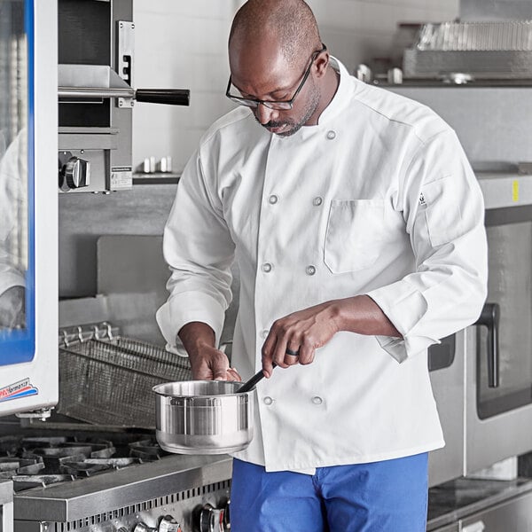 A man in a white Uncommon Chef long sleeve coat cooking in a kitchen.