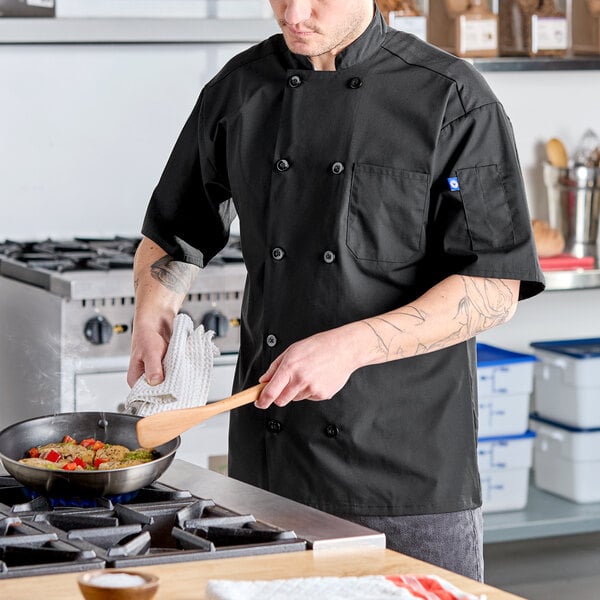 A black short sleeve chef coat with a mesh back, worn by a person cooking in a kitchen.