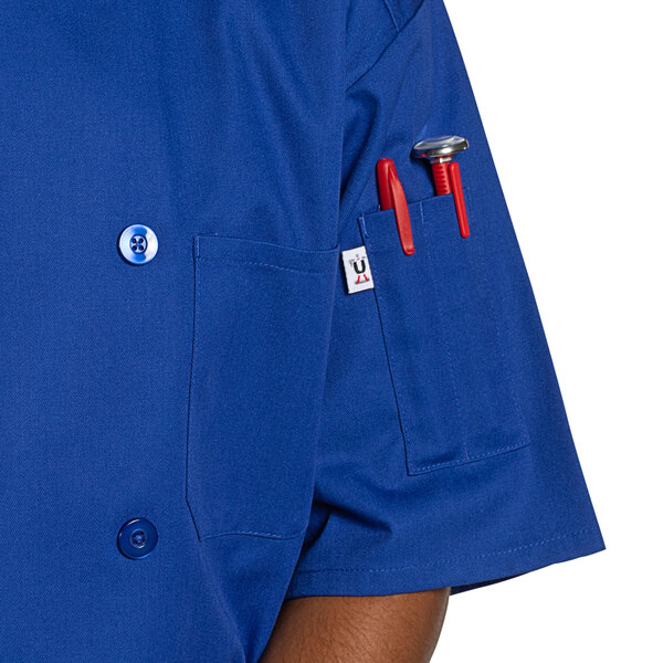 A man wearing a royal blue short sleeve chef coat with red buttons.