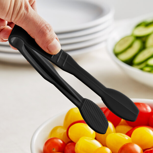 A person holding Thunder Group black flat grip tongs over a bowl of tomatoes.