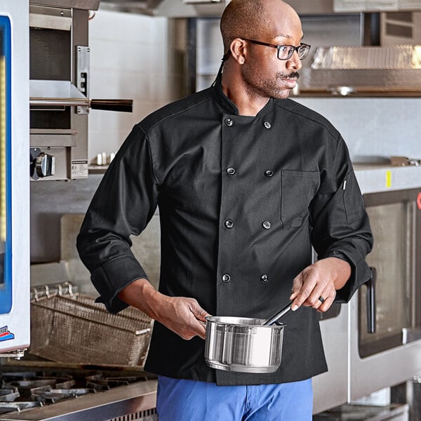 A man in a black Uncommon Chef long sleeve chef coat holding a pot.