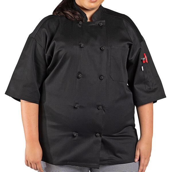 A woman wearing a black Uncommon Chef short sleeve chef coat. The coat has a mesh back.