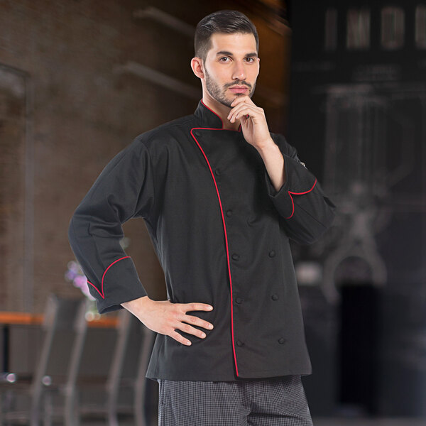 A man wearing a Uncommon Chef black chef coat with red piping.
