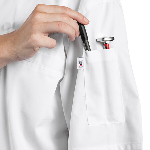 A person in a white Uncommon Chef Aruba Pro Vent short sleeve chef coat with a pen in the pocket.