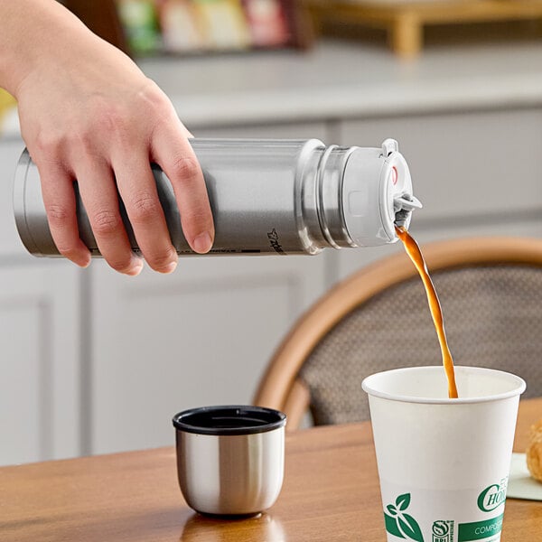A hand pouring coffee from a Zojirushi stainless steel bottle into a mug.