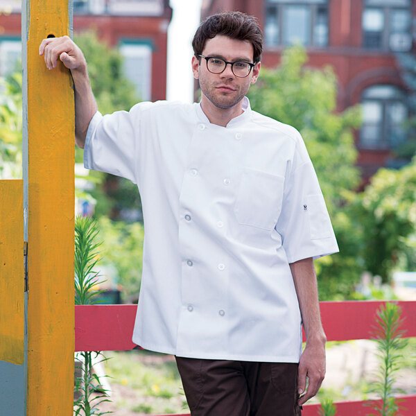 A man wearing a white Uncommon Chef Montego Pro Vent short sleeve chef coat with mesh back.
