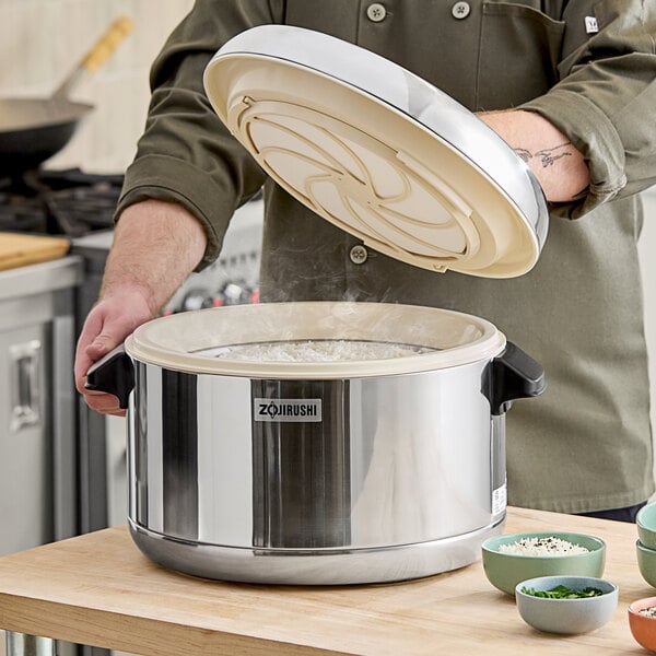 A person using a Zojirushi stainless steel rice container to cook rice.