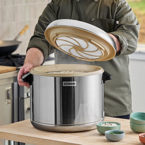 A person using a Zojirushi stainless steel rice container to prepare sushi rice.